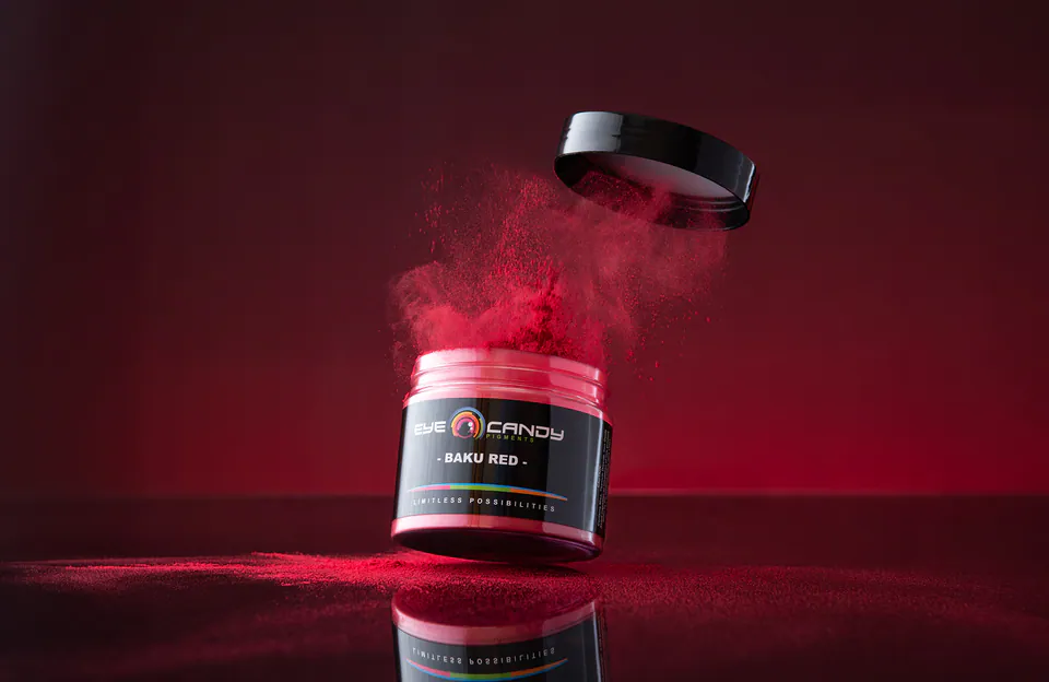Commercial product photograph of a red Eye Candy Pigments jar suspended above a reflective surface
