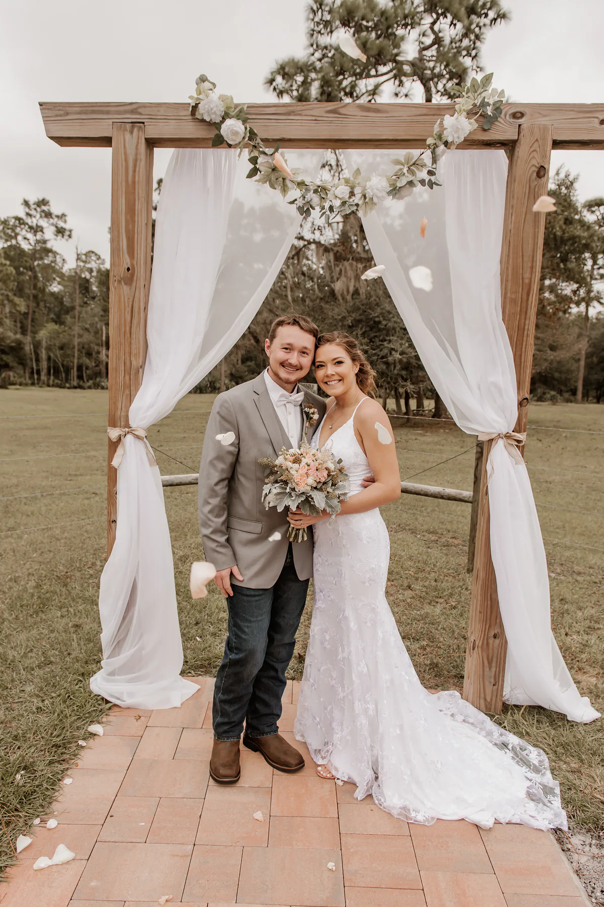 Newlyweds beneath a wooden ceremony arch draped in white fabric at Diamond L Venue